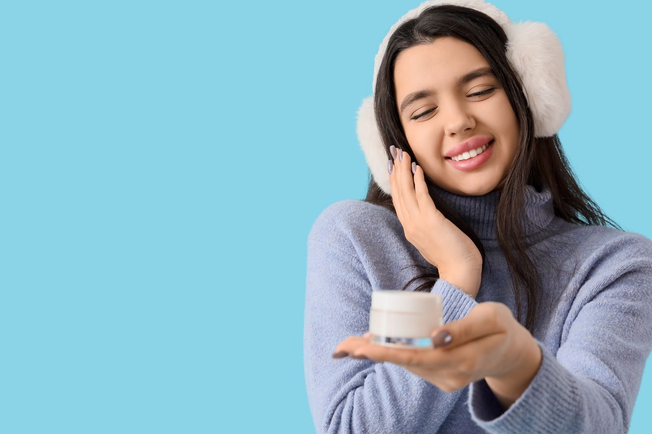 Jeune femme en pull d’hiver tenant un pot de crème pour le visage