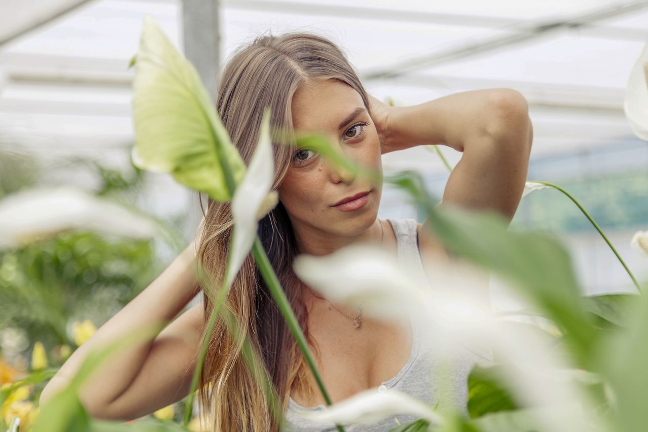 Jeune femme aux cheveux châtains attachés, tablier de lin, plantes séchées et flacons en arrière-plan
