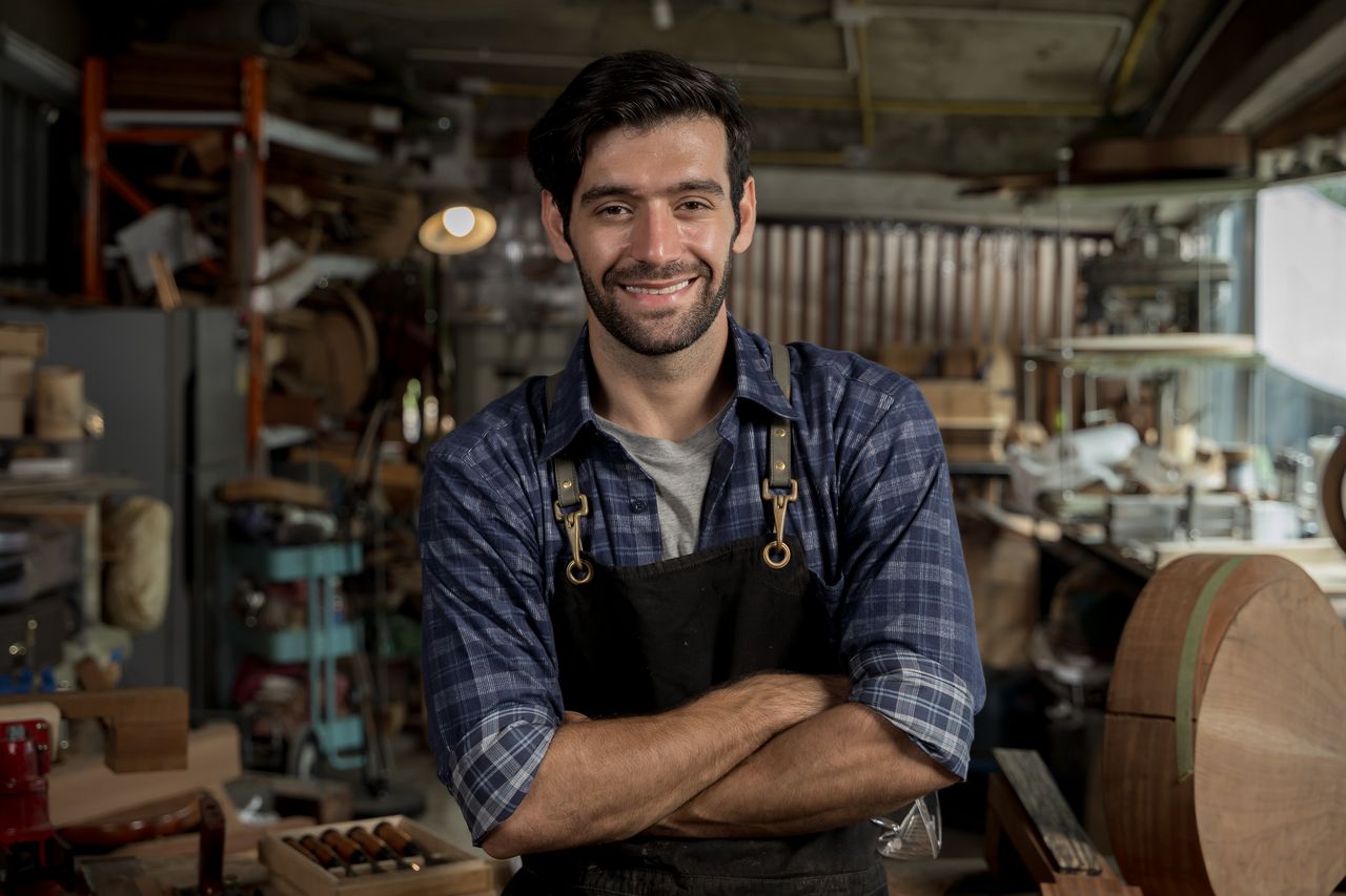 Homme d'une cinquantaine d'années en chemise de travail, sourire tranquille, atelier lumineux en fond