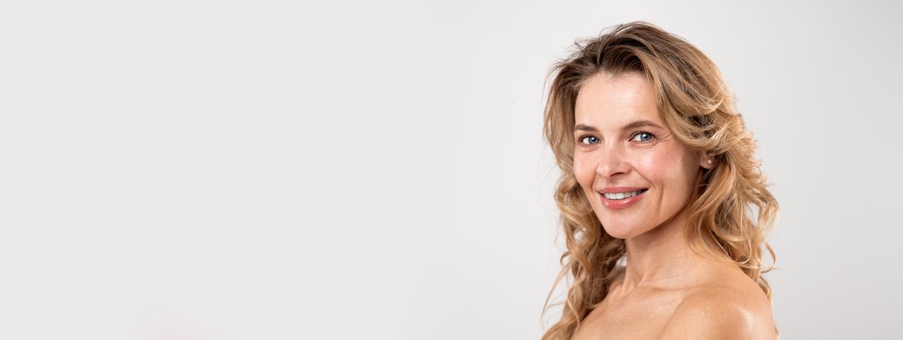 Femme brune d'une quarantaine d'années au sourire franc, chemise claire, lumière douce de salon de soins